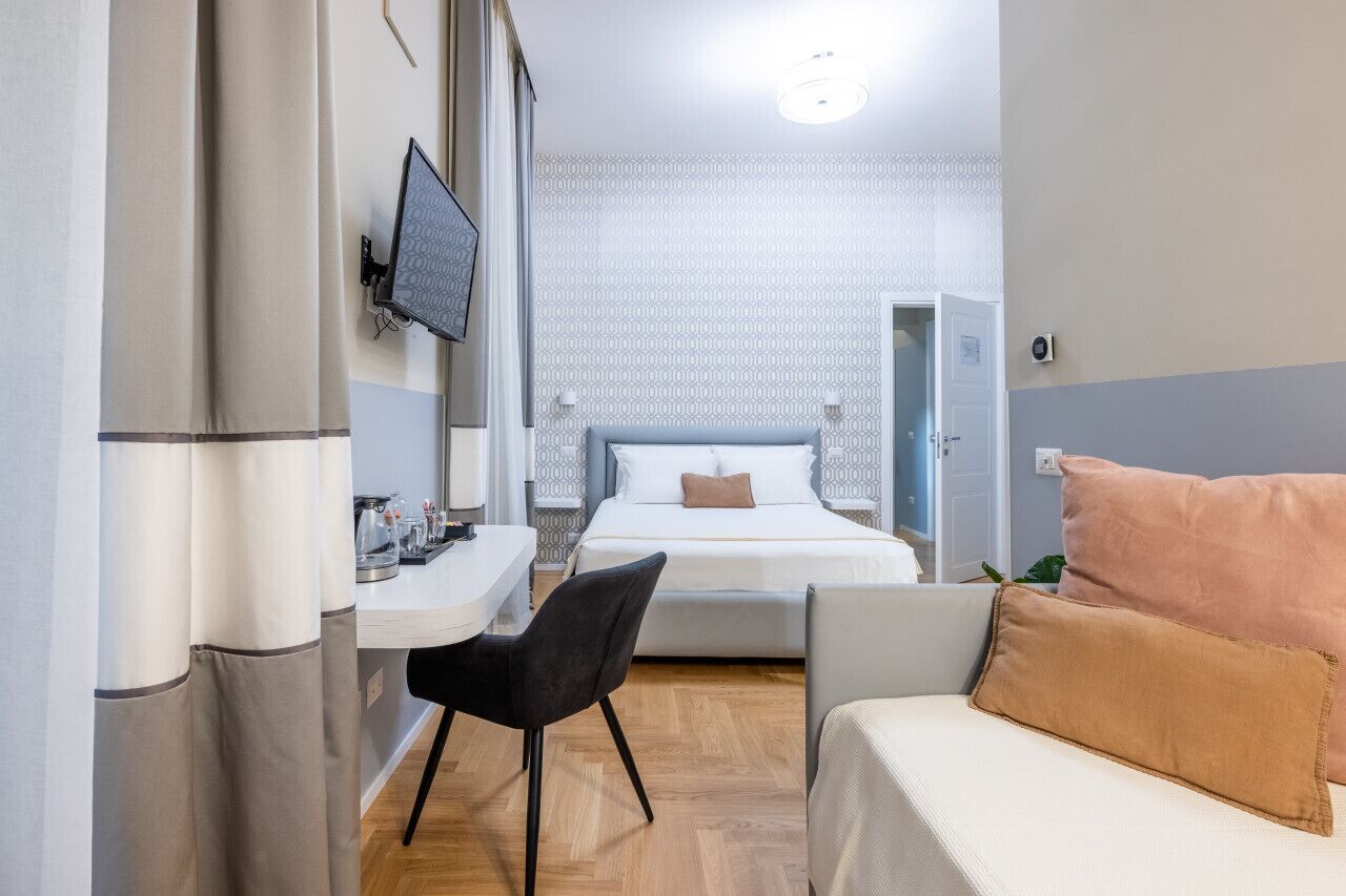 A compact hotel room with a bed, a desk, a chair, and a sofa.