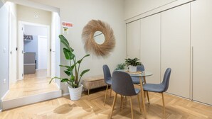 A modern dining area with a round table, two grey chairs, and a potted plant. - Tiberia Room - Suites Romae Rex (Roma)