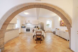A spacious kitchen with an archway, white cabinets, a dining table set for four, and a tiled floor.
