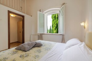Een slaapkamer met een bed, een raam met uitzicht op bomen, een deur en een lamp.
