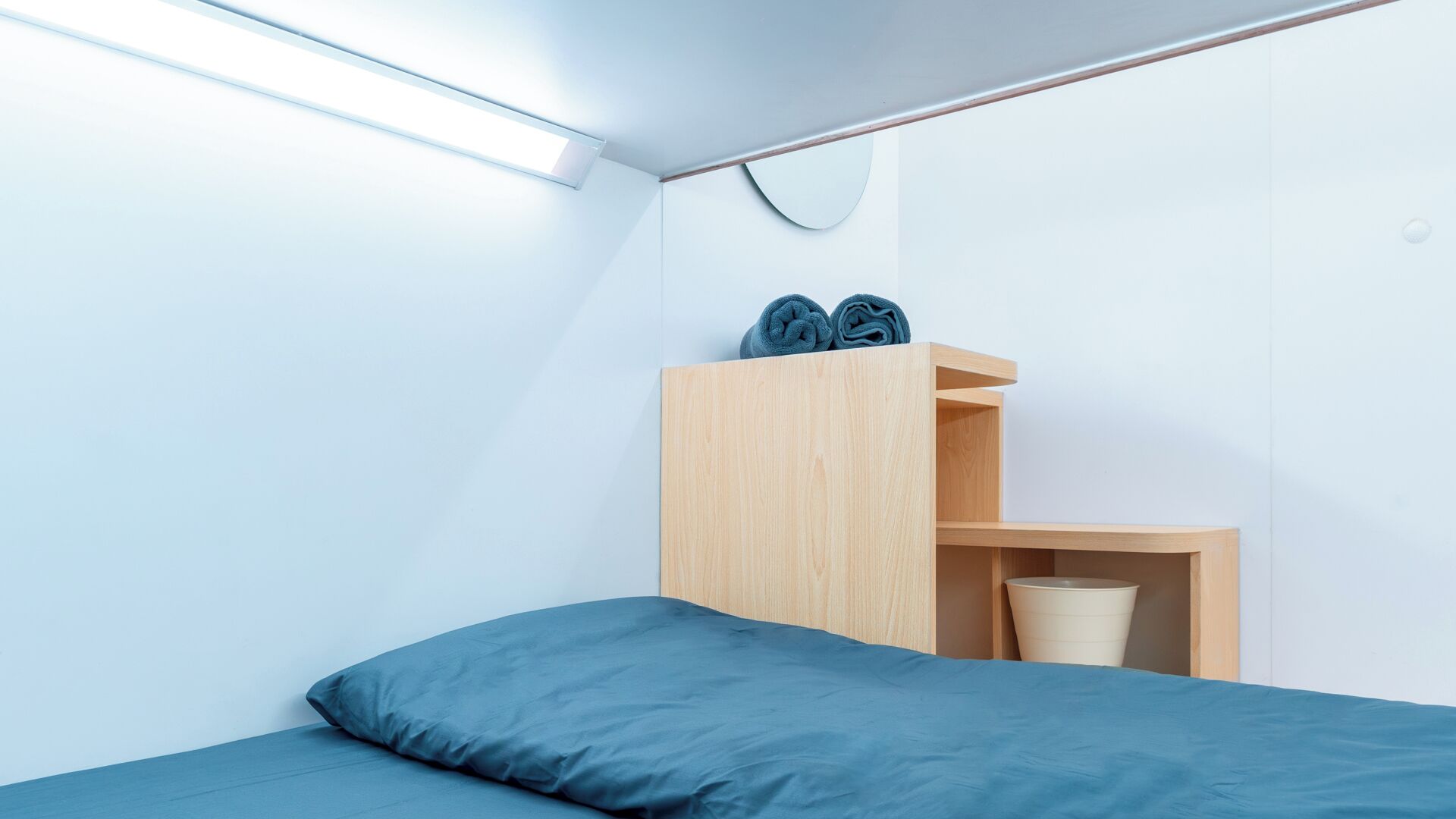 Una camera da letto minimalista con un letto, un armadio in legno e una piccola mensola.