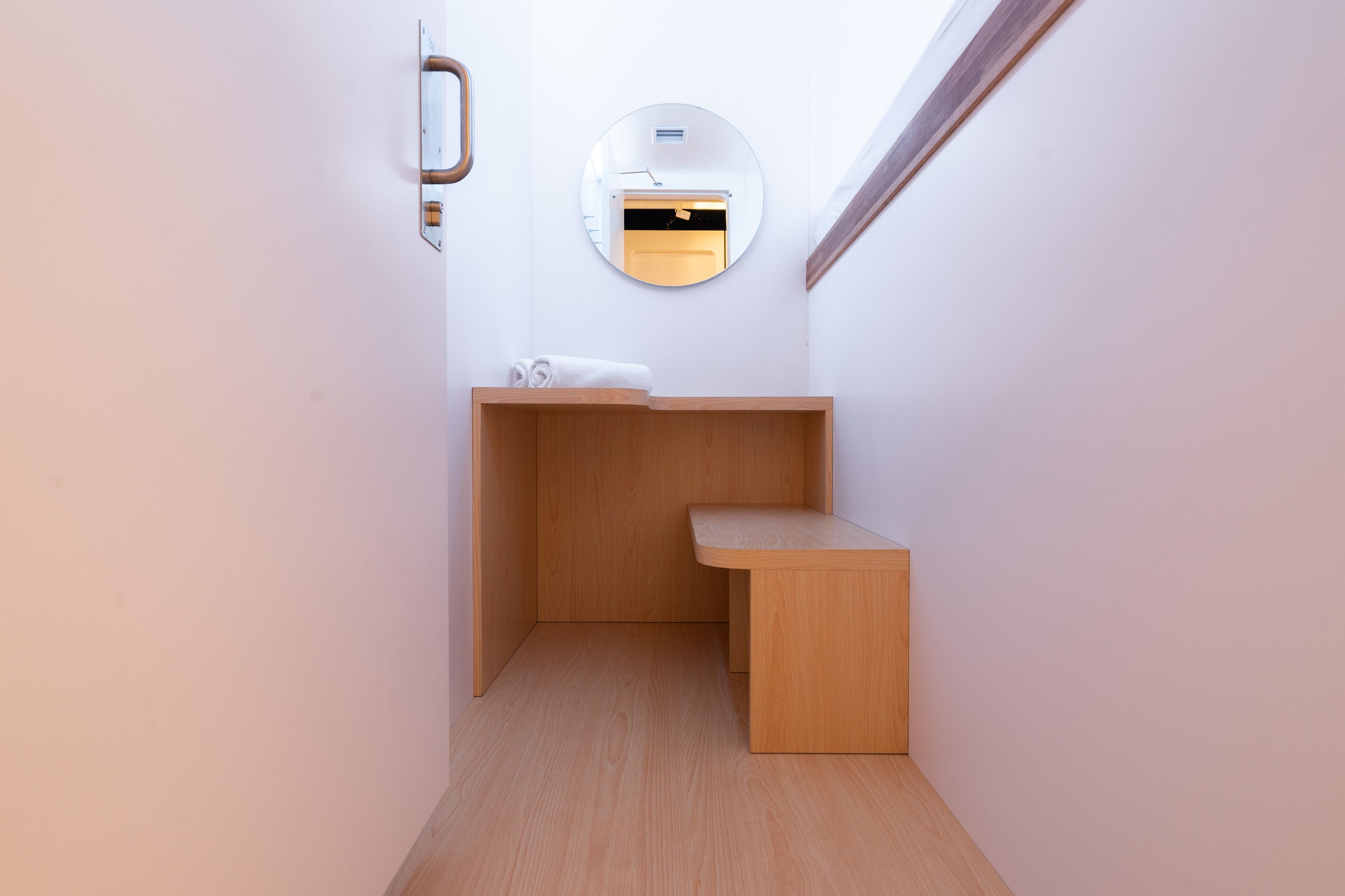 A small, compact bathroom with a wooden vanity, a round mirror, and a towel on the counter.