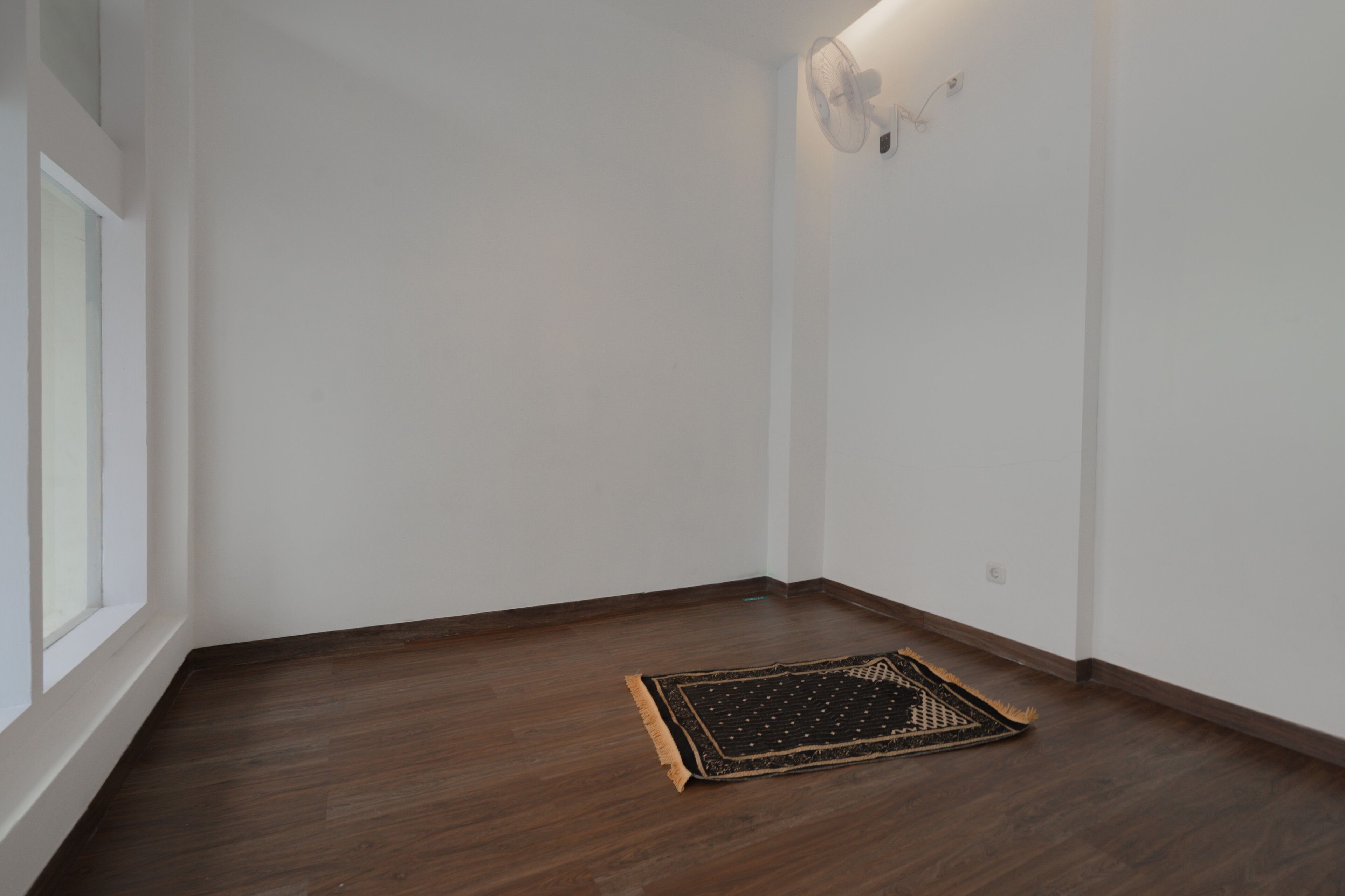 A room with a dark wooden floor, a black and beige rug, and a white wall with a ceiling fan.