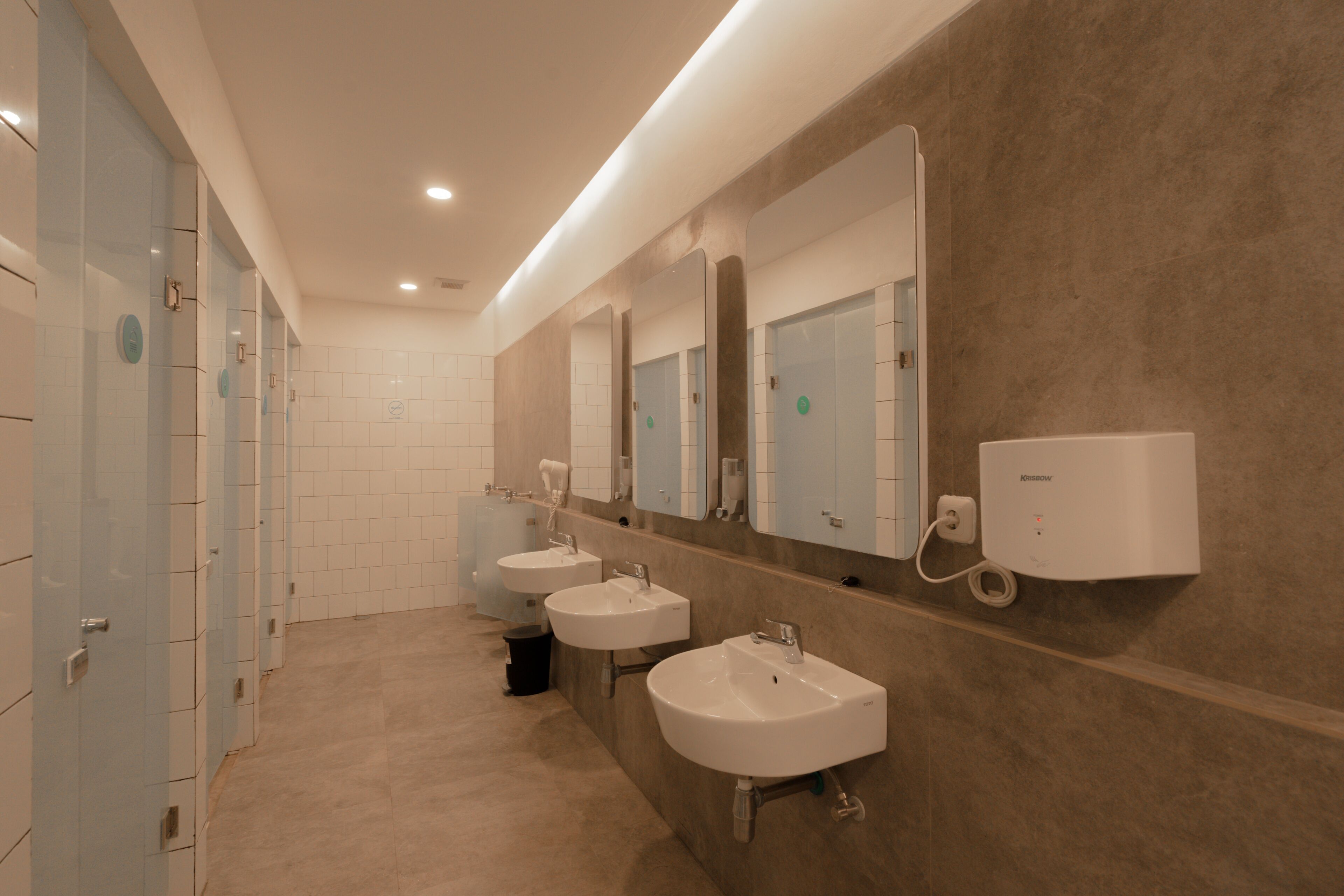Ein modernes Badezimmer mit drei Waschbecken, einem großen Spiegel und einem an der Wand montierten Luftreiniger.