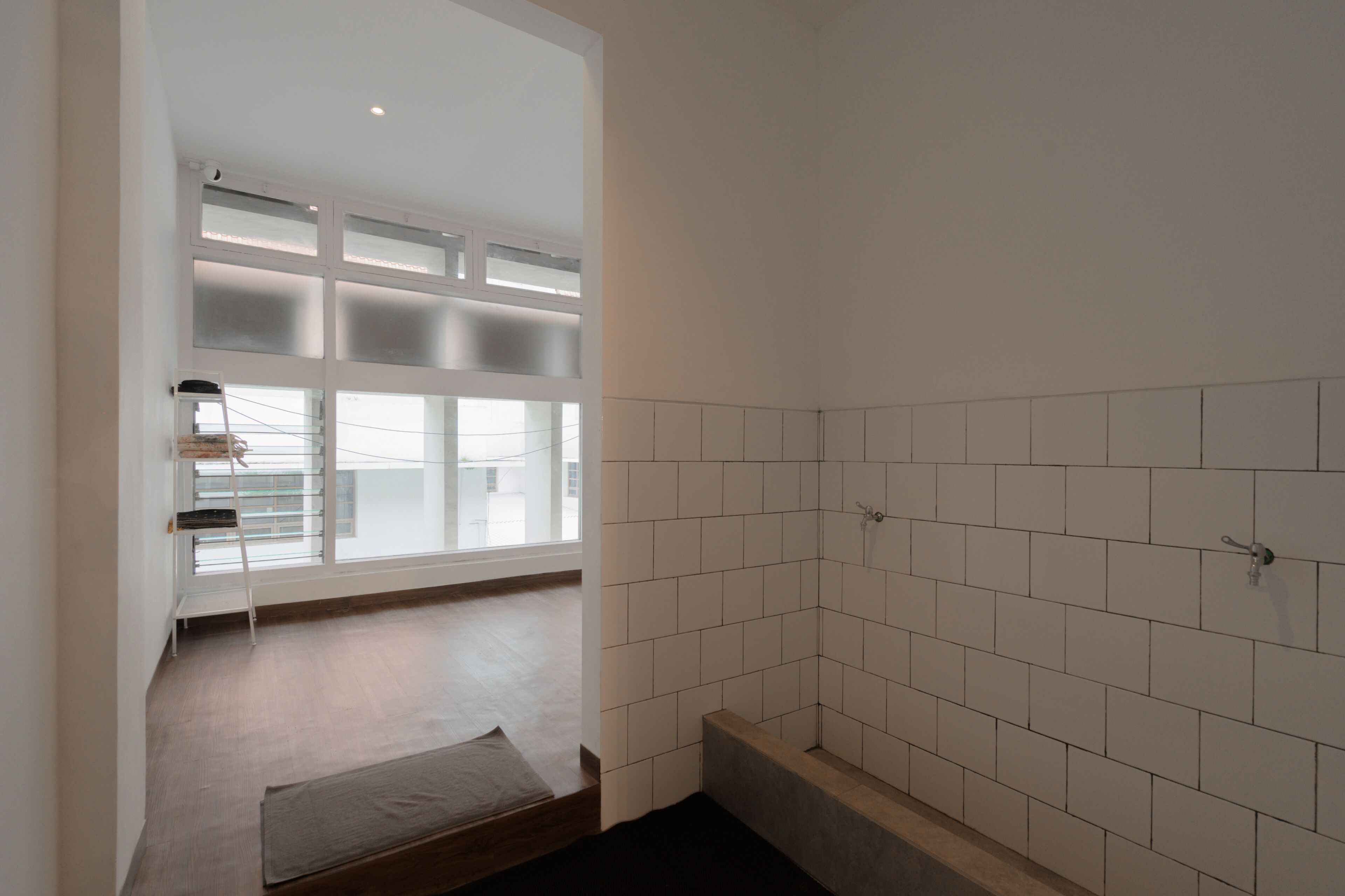 A bathroom with white tiles, a wooden bench, and a window with blinds.
