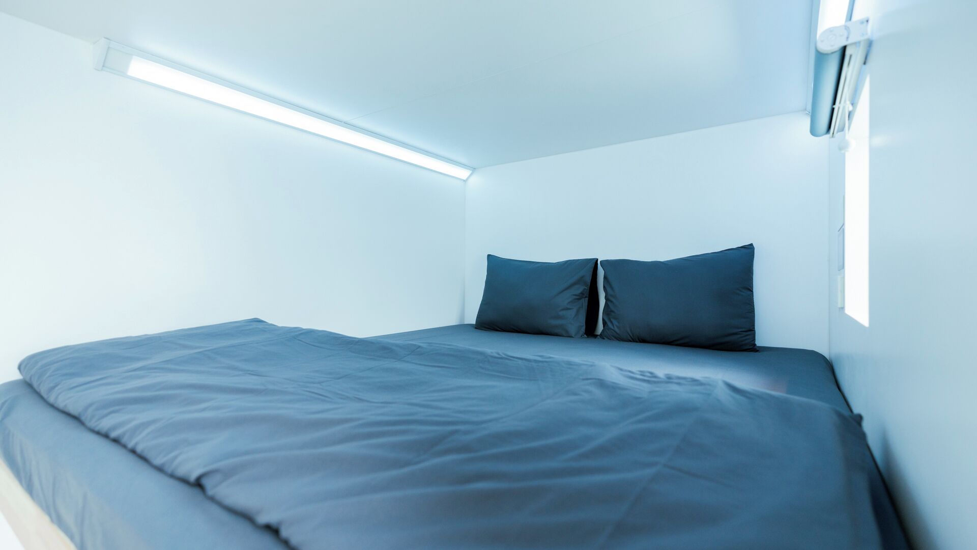 A small, modern room with a single bed, a ceiling light, and a window.