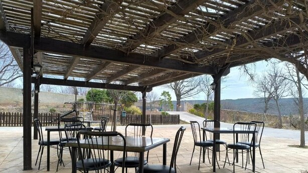 An outdoor patio with tables and chairs, a pergola overhead, and a view of a hilly landscape.