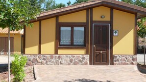 A yellow building with a brown door and window, stone base, and a paved entrance.