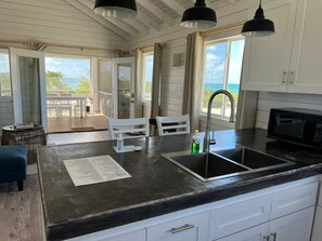 A kitchen with a black countertop, white cabinets, a stainless steel sink, and a black microwave.