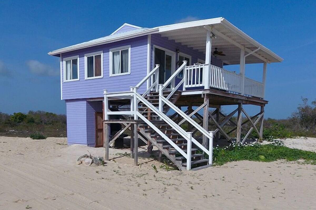 A beach house with a two-story structure, a balcony on the upper floor, and a staircase leading to the entrance.