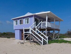 A beach house with a two-story structure, a balcony on the upper floor, and a staircase leading to the entrance.