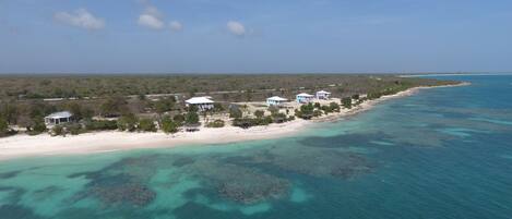 An aerial view of a coastal property with several white buildings, a sandy beach, and clear turquoise waters.