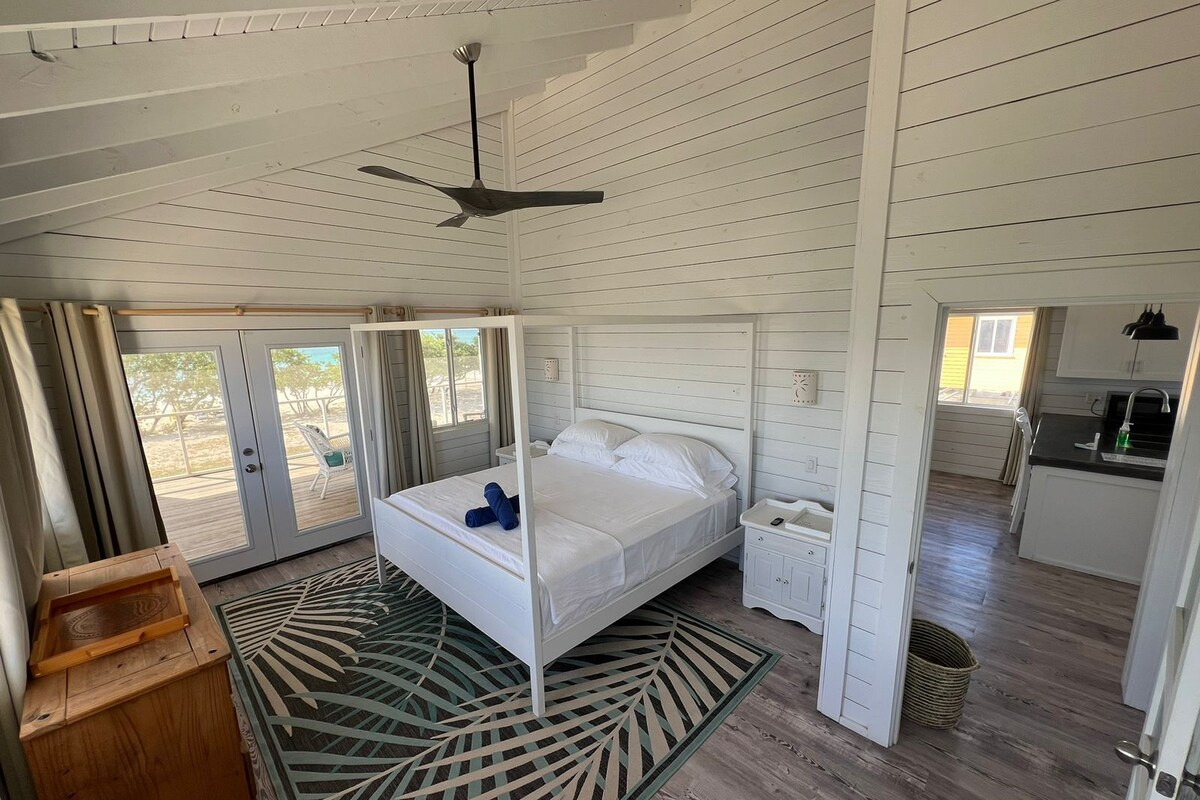 A bedroom with a bed, a bedside table, a nightstand, a ceiling fan, and a view through a sliding door to a balcony.