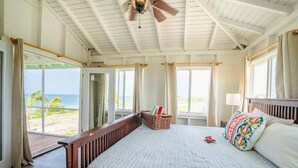 Ein Schlafzimmer mit einem großen Bett, einem Deckenventilator und Blick auf den Strand.