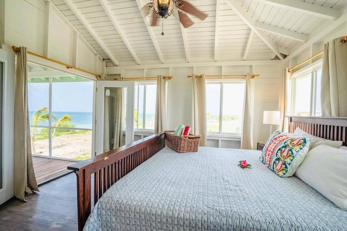 A bedroom with a large bed, a ceiling fan, and a view of the beach.