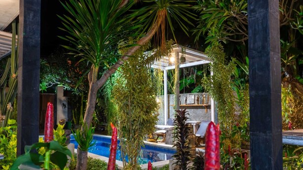 Un espace piscine agrémenté d’un belvédère, entouré d’une végétation luxuriante et de plantes aux couleurs vives.