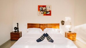 Un lit bien fait, avec des draps blancs, une tête de lit en bois et une paire de chaussettes posées en travers au pied du lit.