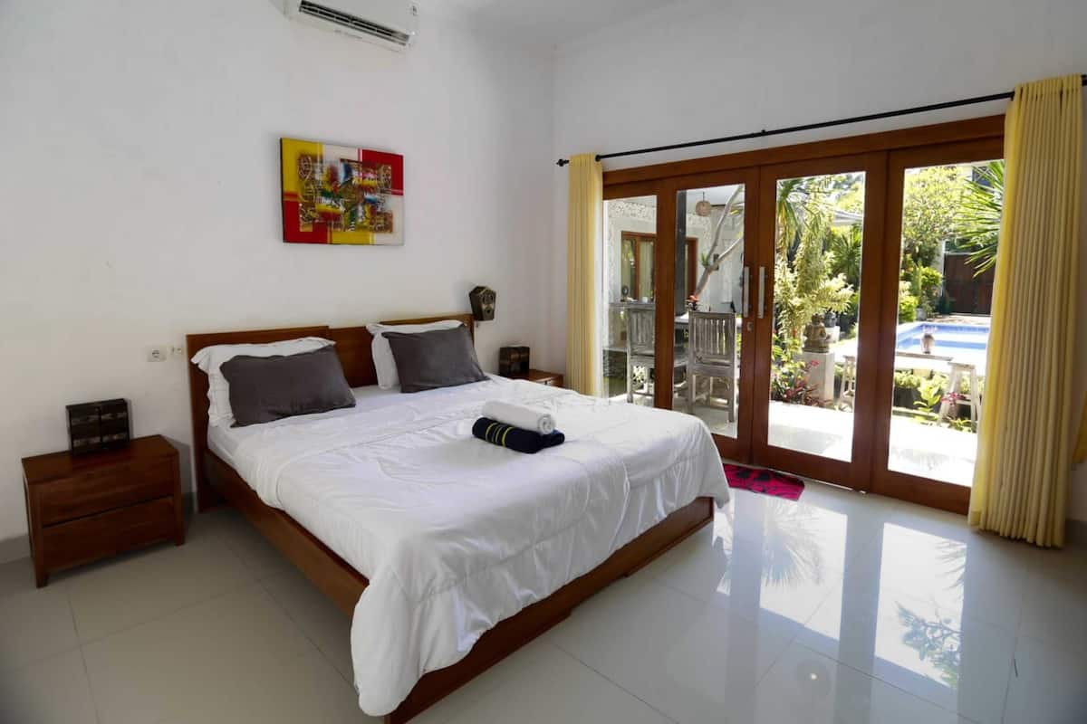 A bedroom with a large bed, wooden headboard, and a view of a garden through a sliding glass door.