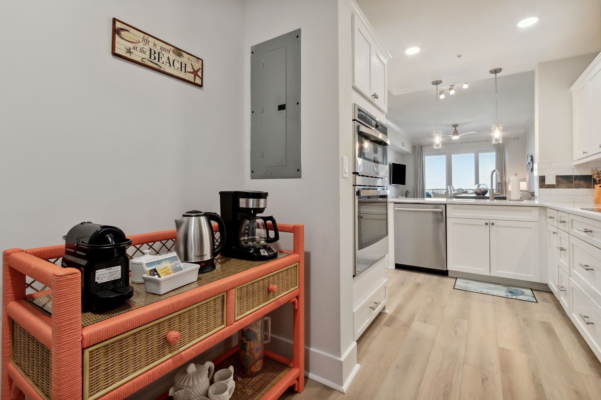Una cocina moderna con gabinetes blancos, electrodomésticos de acero inoxidable y un carrito auxiliar de mimbre.