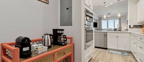 Una cocina moderna con gabinetes blancos, electrodomésticos de acero inoxidable y un carrito auxiliar de mimbre.
