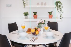 A round dining table with white plates, bowls, and cutlery, surrounded by black chairs.