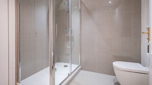 A modern bathroom with a glass-enclosed shower, a white toilet, and tiled walls.