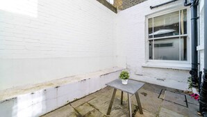 A small outdoor area with a white brick wall, a window, and a table with a potted plant. - 2BR 2BA near Hyde Park & Kensington (London)