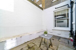 A small outdoor area with a white brick wall, a window, and a table with a potted plant. - 2BR 2BA near Hyde Park & Kensington (London)