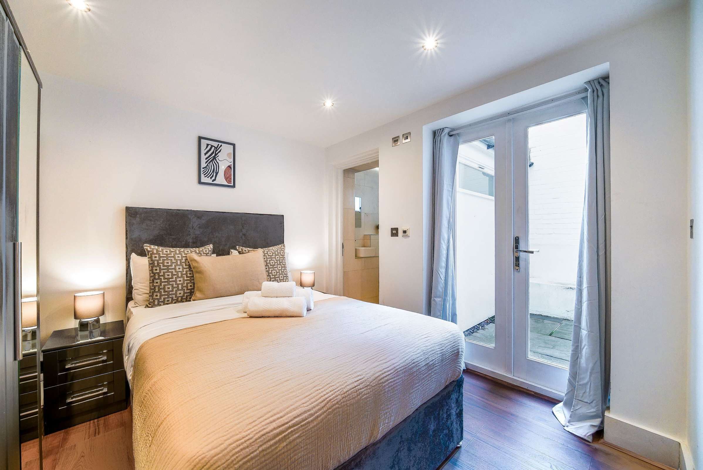 A hotel room with a large bed, bedside lamps, a headboard, and a door leading to a balcony.