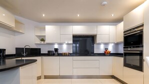 A modern kitchen with white cabinets, a black countertop, and built-in appliances including a stove and oven. - 2BR 2BA near Hyde Park & Kensington (London)