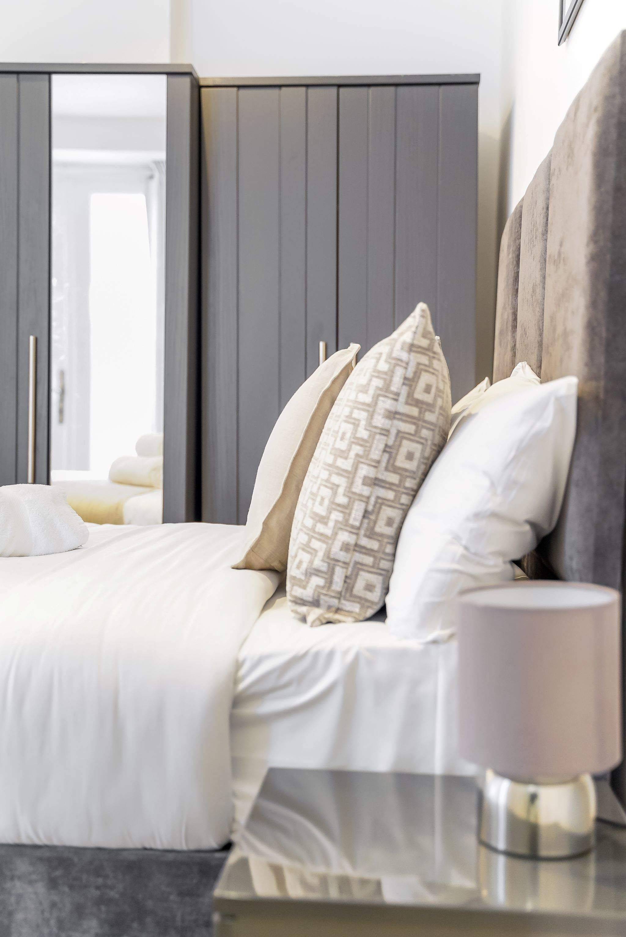 Une chambre à coucher moderne avec un lit, des oreillers, une table de chevet et une commode.