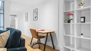Ein modernes Wohnzimmer mit einem dunkelblauen Sofa, einem Holztisch mit Stuhl, weißen Regalen und zwei gerahmten Kunstwerken an der Wand.