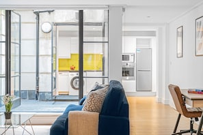 A modern living space with a sofa, a dining table, and a kitchen area visible through glass doors.