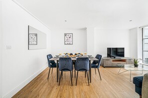 A modern dining area with a wooden floor, a dining table with chairs, a TV, and artwork on the walls. - Modern 2-Bedroom in the Heart of Holborn (London)