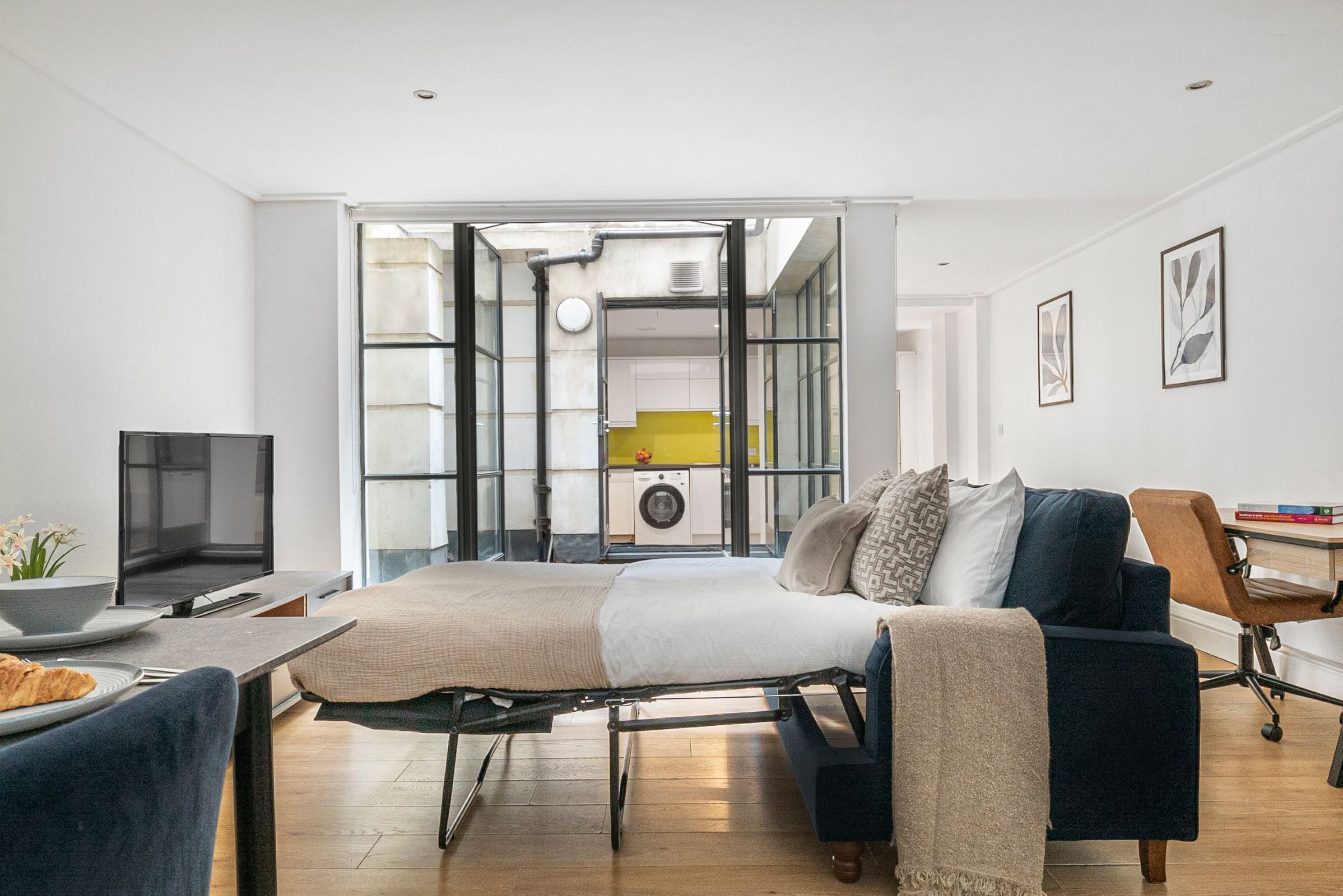 A modern living room with a bed, a TV, and a dining area.