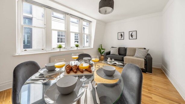 Ein modernes Wohnzimmer mit Essbereich, großen Fenstern und einer Couch.