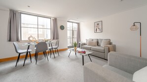 A modern living room with a dining area, grey sofas, a coffee table, and a large window with curtains. - Spacious 2-Bedroom Flat in London's Holborn (London)