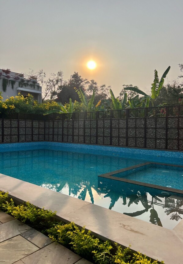 Una piscina con borde de azulejos, rodeada por un bajo muro de piedra y abundante vegetación.