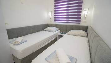 A twin room with two single beds, a small table, and a window with purple blinds.
