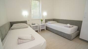 A bedroom with two single beds, a nightstand with a vase, and a window with blinds.