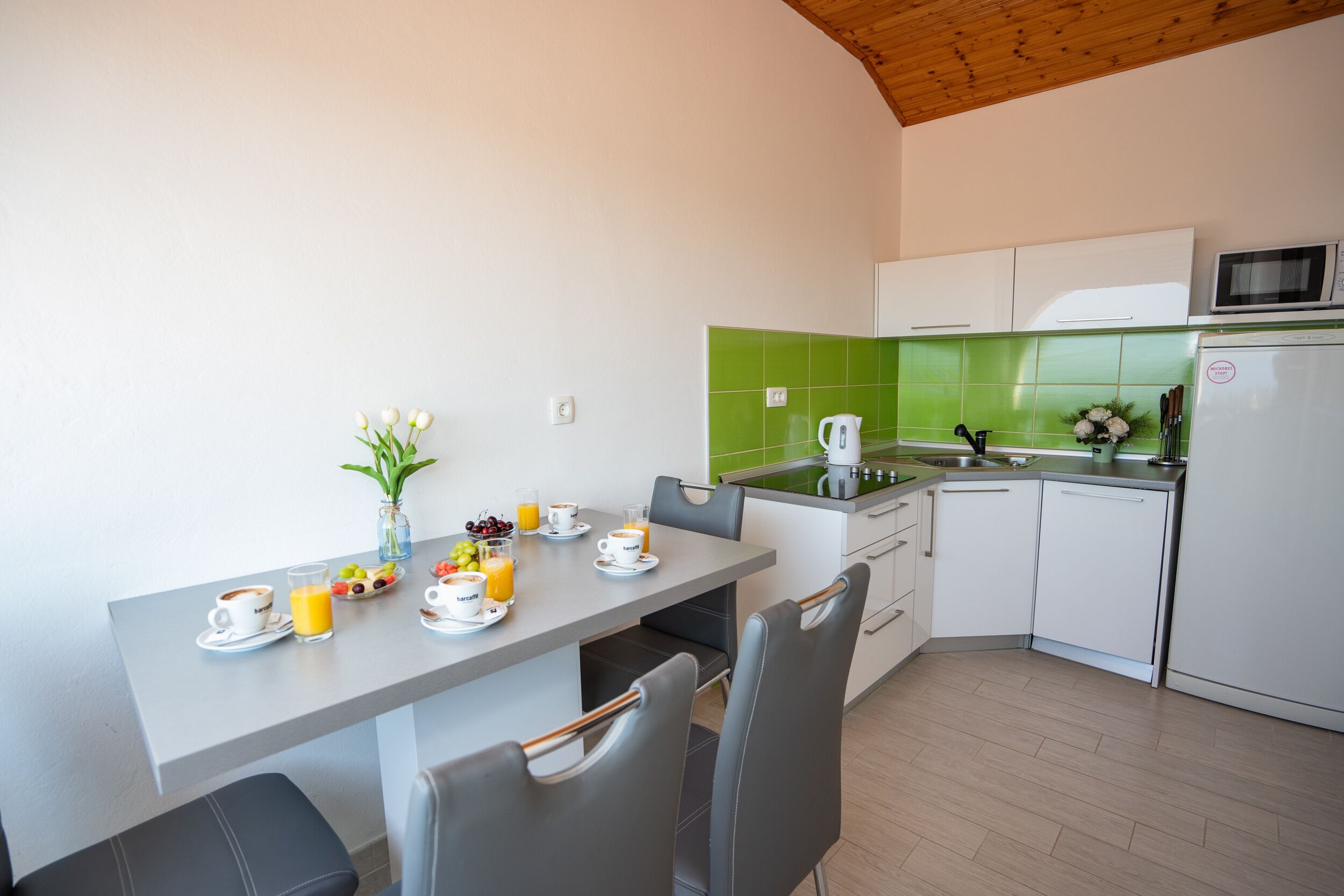 Uma cozinha moderna com armários brancos, painel de fundo verde e um espaço de jantar com mesa posta para o café da manhã.