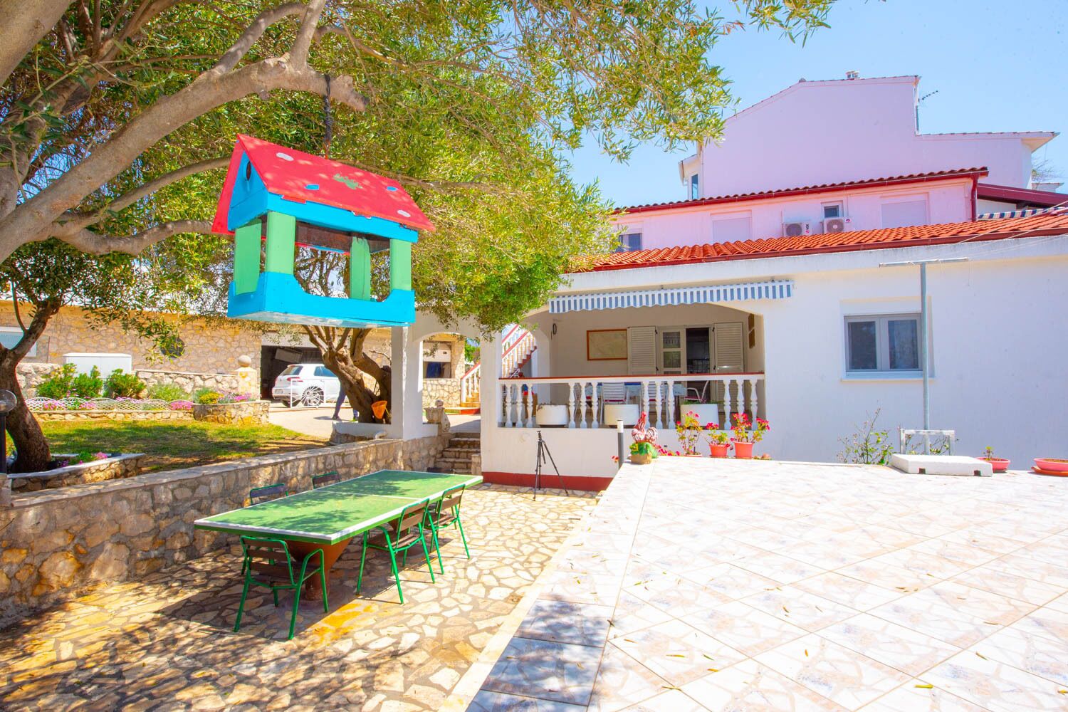 A courtyard with a table and chairs, a small playhouse, and a building with a red-tiled roof.