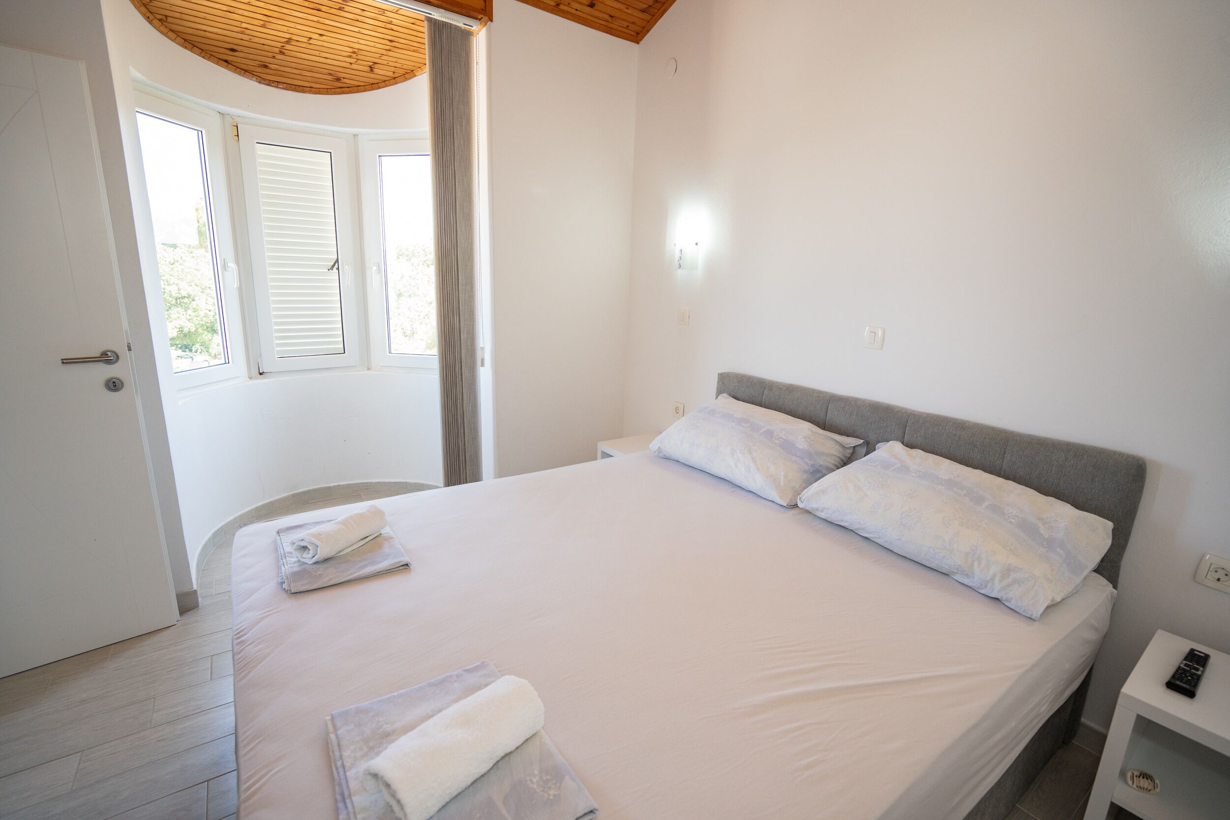 Ein Schlafzimmer mit einem Bett, einem Nachttisch, einer Tür und einem Fenster mit Rollläden.