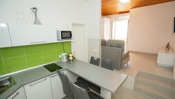 A modern kitchen with a grey countertop, white cabinets, and a green backsplash. There is a microwave on the countertop, a sink, and a chair.