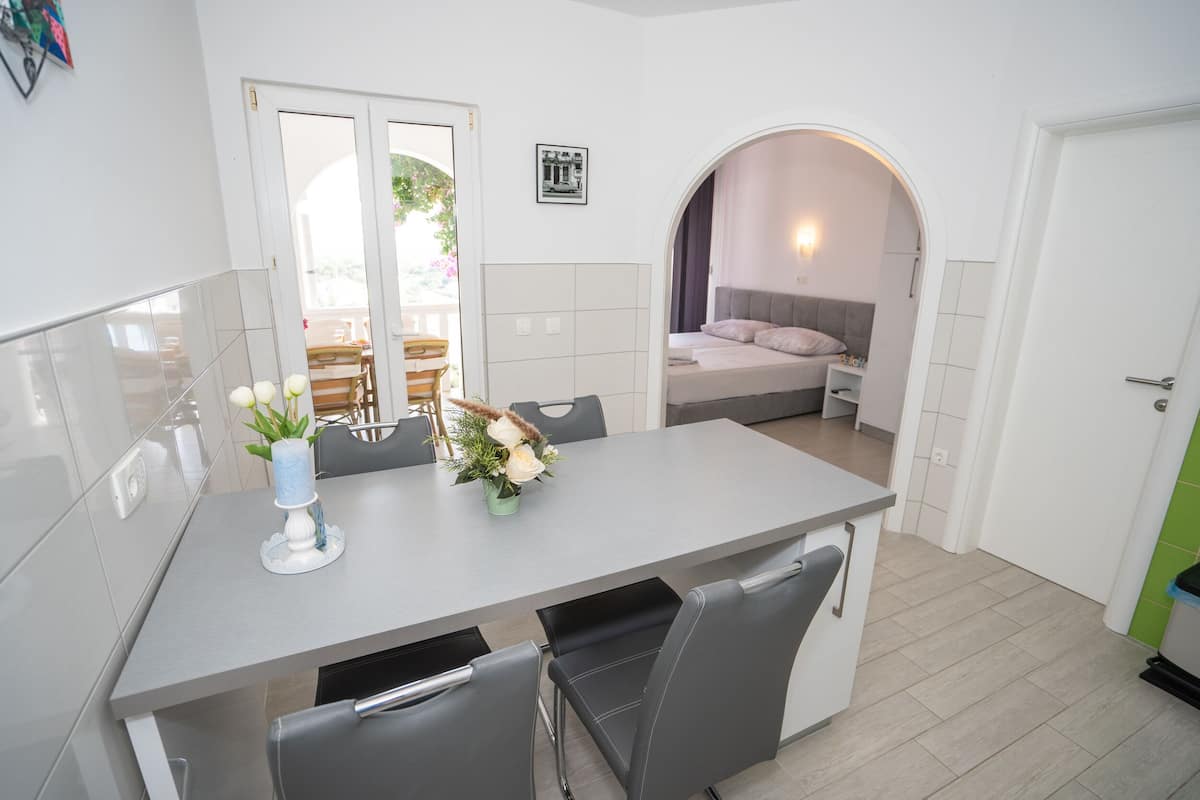 Une cuisine compacte avec un coin repas, une petite chambre avec un lit et une table de chevet, et une salle de bain visible à travers une arche.