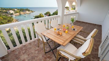 A terrace with a wooden table, white cushioned chairs, and a view of the sea.