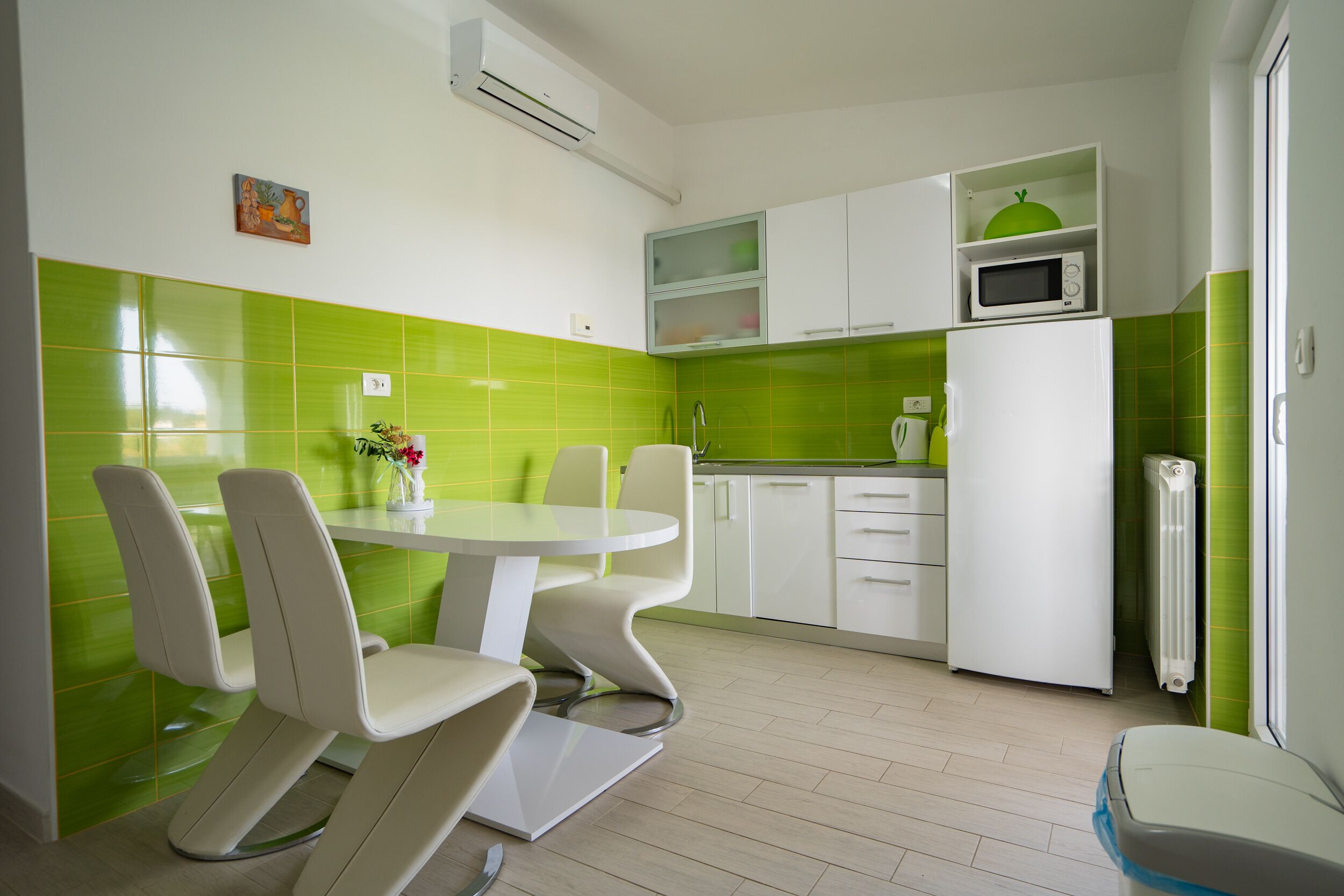 Une cuisine moderne avec une table ronde et des chaises blanches, des carreaux verts sur le mur derrière l’évier et des armoires blanches.