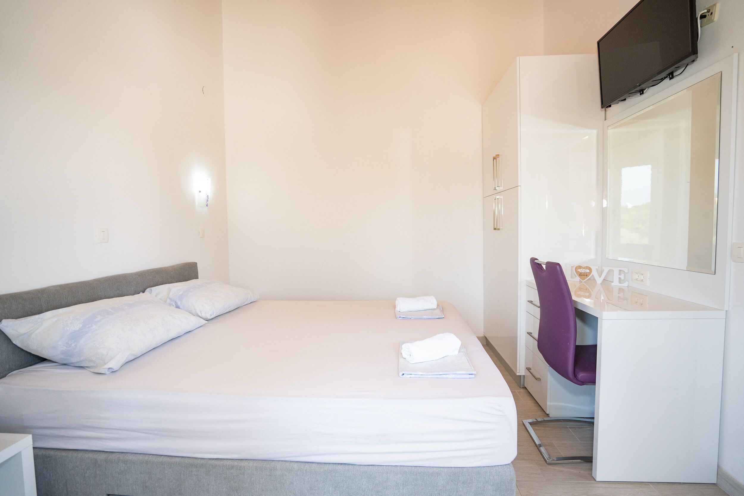 Un dormitorio con cama, escritorio y televisor montado en la pared.