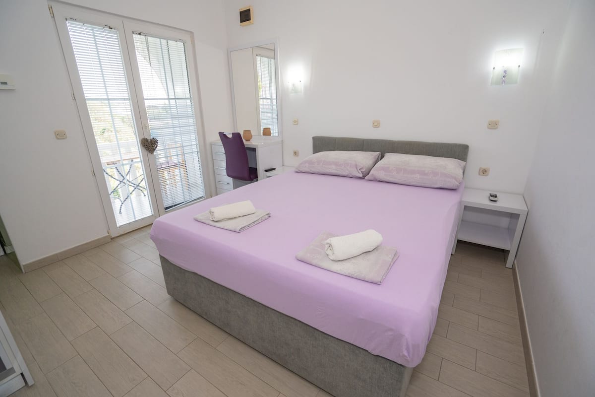 Une chambre à coucher comprenant un lit, deux tables de chevet, un bureau avec une chaise et une porte-fenêtre coulissante donnant sur un balcon.