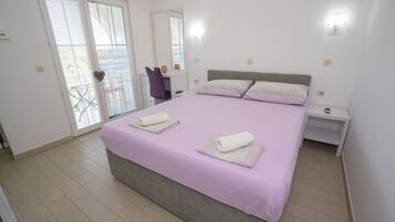 A bedroom with a bed, two nightstands, a desk with a chair, and a sliding glass door leading to a balcony.
